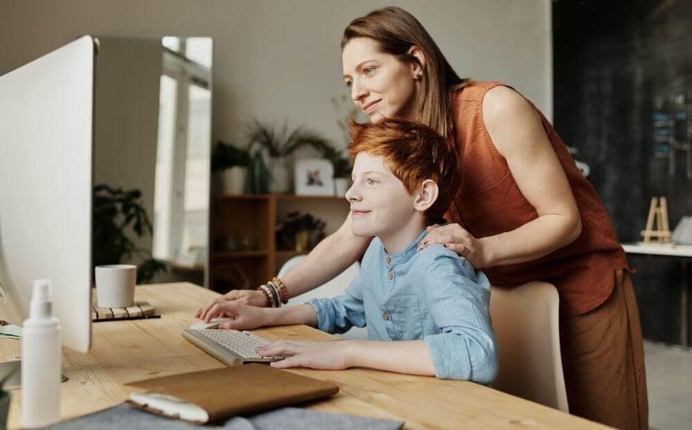 female teacher helping a young male student learn how to code on a computer